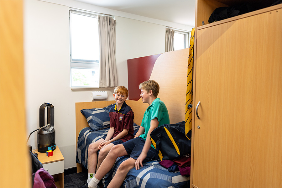 Two Middle School boarders sitting on a bed laughing in the College's boarding house.